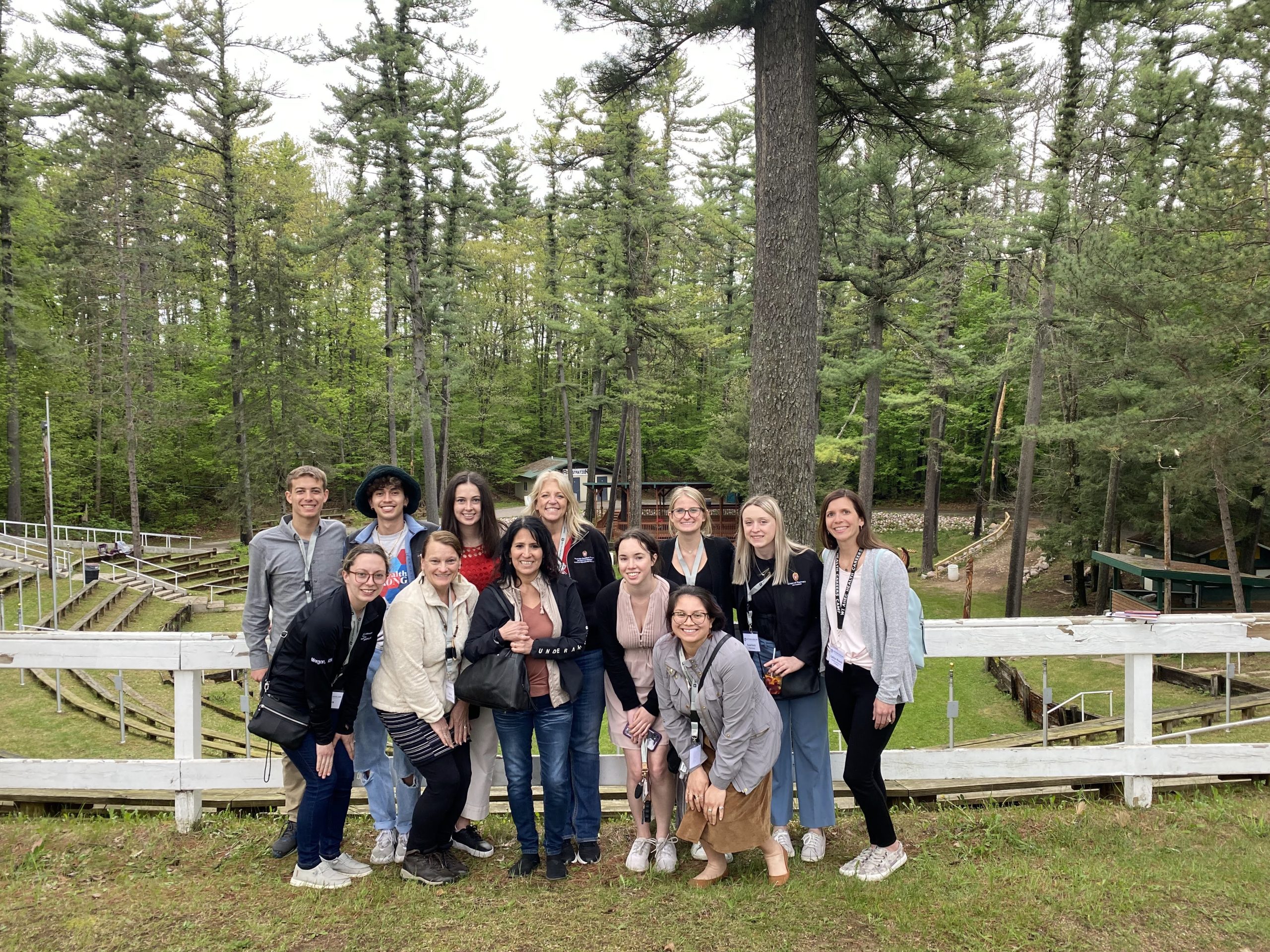 A group of AHEC Scholars stand smiling in front of tall pine trees