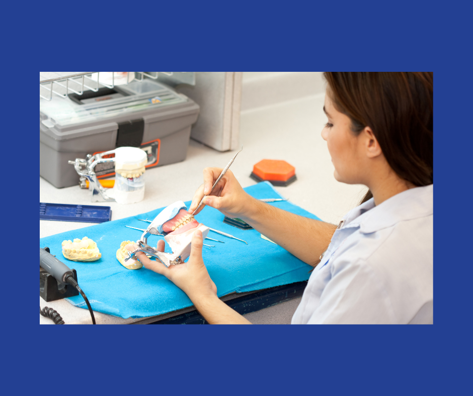 A lab tech in a white coat uses a dental tool on a set of dentures in a lab