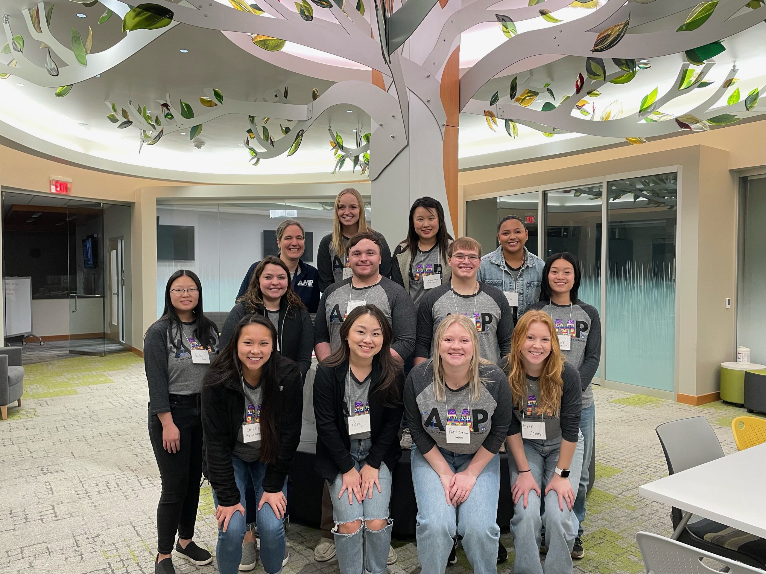 Thirteen AMP participants in grey shirts with the AMP logo pose and smile
