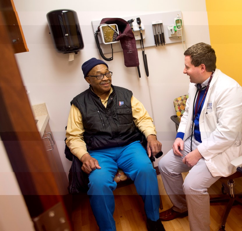 A man sits in an exam room talking with a doctor, both are smiling