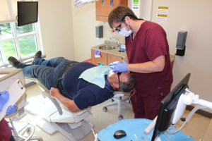 A dental technician performs an exam on a patient reclining in a chair