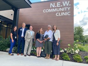 Smiling people stand outside of a building with a sign that reads, "N.E.W. Community Clinic"