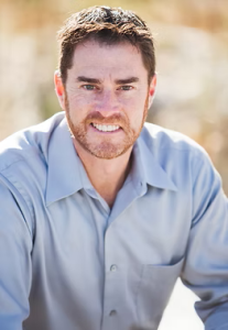 A man with dark hair in a blue button-up shirt smiling