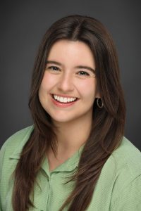 A woman with long brown hair and a green shirt smiling