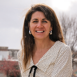 A woman smiling with long brown hair and a white and black polka-dot blouse